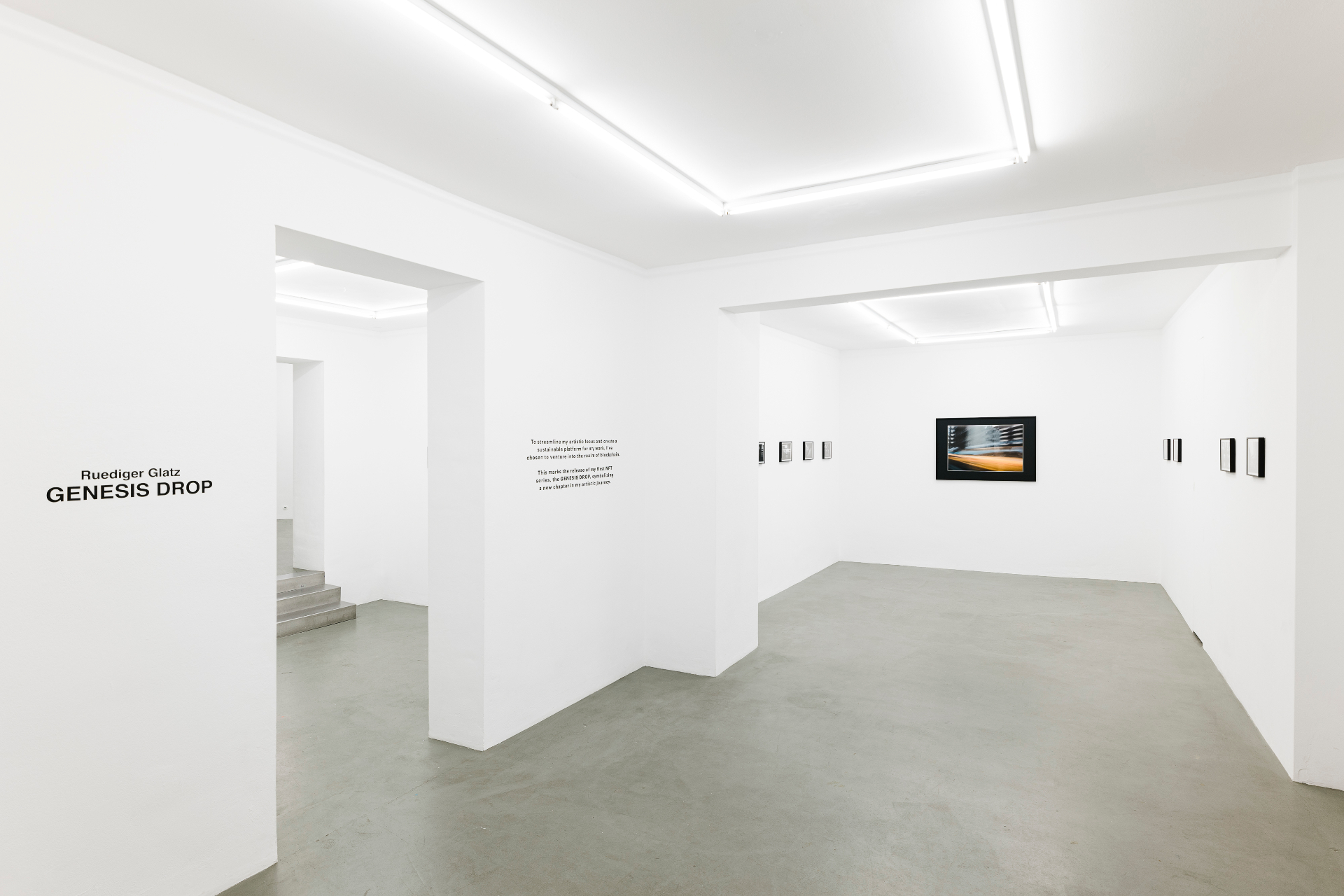 Installation view — GENESIS DROP wall with framed works and mirrored reflections